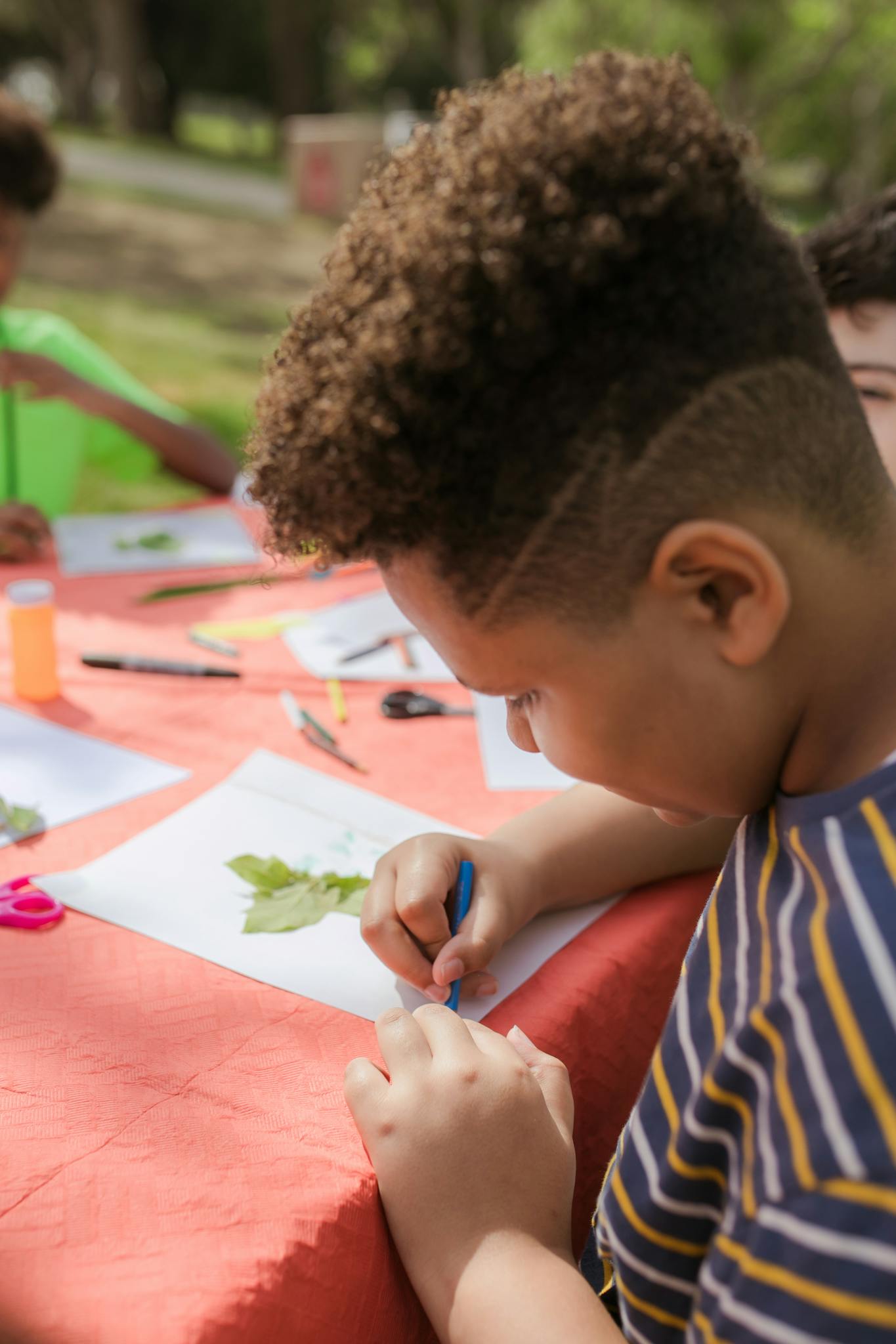 A young boy engaged in a drawing activity at an outdoor table with friends.