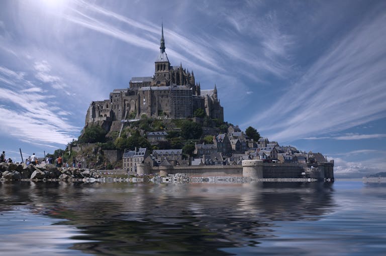 A picturesque view of the historic Mont Saint-Michel reflecting in the water under a bright sky.